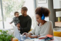 Father holding baby daughter behind working mother at laptop — Stock Photo
