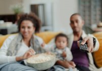 Famille avec télécommande regarder la télévision avec pop-corn sur le canapé — Photo de stock