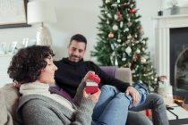 Дружина відкриває різдвяний подарунок від чоловіка на дивані у вітальні — стокове фото