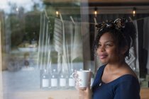 Femme réfléchie propriétaire de magasin boire du café à la fenêtre du magasin — Photo de stock
