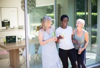 Happy senior women friends drinking and laughing on sunny patio — Stock Photo