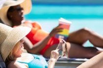 Старша жінка, використовуючи смартфон і сонячні ванни в літньому басейні — стокове фото