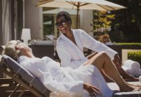Happy senior women friends relaxing in spa robes on sunny hotel patio — Stock Photo