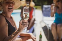 Счастливая пожилая женщина пьет шампанское с друзьями на летнем патио — стоковое фото