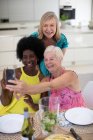 Happy senior women friends in dresses taking selfie at dining table — Stock Photo