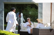 Heureuses femmes âgées amies relaxantes dans des peignoirs de spa sur le patio ensoleillé de l'hôtel — Photo de stock