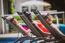 Retrato despreocupado seniores mulheres amigos tomando banho de sol na piscina ensolarada — Fotografia de Stock