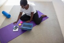 Mulher madura pagando contas e trabalhando no laptop no tapete de ioga — Fotografia de Stock