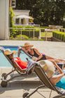 Happy senior women friends sunbathing at sunny summer poolside — Stock Photo