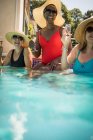 Felices amigas mayores bebiendo champán en la soleada piscina - foto de stock