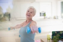 Retrato confiante sênior mulher exercitando com halteres na cozinha — Fotografia de Stock