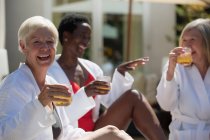 Feliz mujer mayor disfrutando de un cóctel con amigos en el soleado patio del hotel - foto de stock