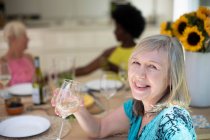 Портрет щаслива старша жінка п'є біле вино з друзями за столом — стокове фото