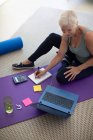 Mulher sênior trabalhando no laptop no tapete de ioga — Fotografia de Stock