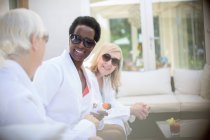 Donne anziane amiche con occhiali da sole e accappatoi termali sul patio dell'hotel — Foto stock