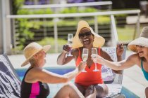 Happy senior women friends drinking champagne at sunny summer poolside — Stock Photo