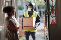 Mujer recibiendo paquetes de repartidor hombre en mascarilla en la puerta principal - foto de stock