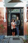 Retrato feliz pareja con bebé hija en casa soleada puerta principal - foto de stock