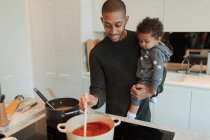 Счастливый отец держит дочку и готовит спагетти на плите — стоковое фото