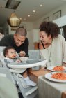 Happy couple feeding baby daughter in high chair — Stock Photo