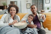 Happy couple with baby daughter watching TV and eating popcorn — Stock Photo