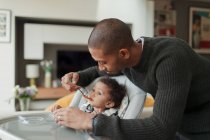 Father feeding baby daughter at high chair — Stock Photo