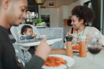 Счастливые родители и маленькая дочь едят спагетти за обеденным столом — стоковое фото