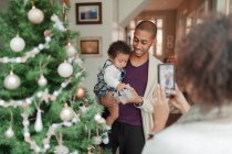 Frau fotografiert Mann und kleine Tochter am Weihnachtsbaum — Stockfoto