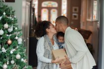 Casal afetuoso com bebê filha beijando na árvore de Natal — Fotografia de Stock