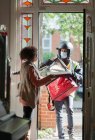 Woman receiving pizza from delivery man in face mask at front door — Stock Photo