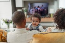 Portrait cute baby girl with parents on living room sofa — Stock Photo