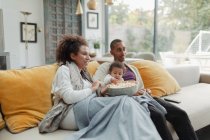 Батьки з дочкою дитина дивиться фільм з попкорном на дивані — стокове фото
