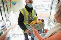 Woman receiving grocery delivery from delivery man in mask — Stock Photo