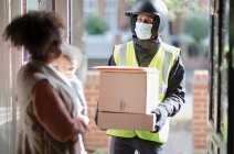 Woman receiving parcels from delivery man in face mask at front door — Stock Photo