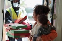 Mãe com bebê filha recebendo pizza de homem de entrega em máscara — Fotografia de Stock