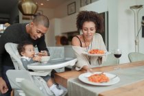 Couple eating spaghetti and feeding baby daughter at dining table — Stock Photo