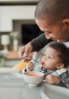 Father feeding cute baby daughter at high chair — Stock Photo