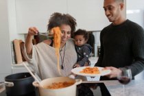 Genitori con bambina che cucinano gli spaghetti al fornello della cucina — Foto stock