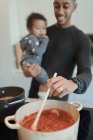 Отец держит дочку и готовит спагетти на плите. — стоковое фото