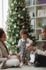 Casal ajudando bebê filha abrir presente de Natal na sala de estar — Fotografia de Stock