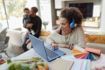 Woman working at laptop with husband and baby daughter in background — Stock Photo