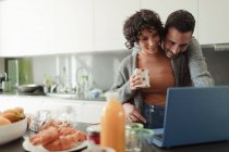 Couple affectueux travaillant à l'ordinateur portable dans la cuisine du matin — Photo de stock