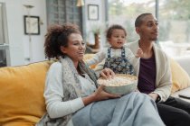 Paar mit kleiner Tochter isst Popcorn und schaut Fernsehen auf dem Sofa — Stockfoto
