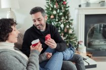 Happy couple opening Christmas gift on living room sofa — Stock Photo