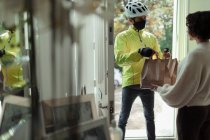 Frau bekommt Essen vom Lieferanten mit Gesichtsmaske vor der Tür — Stockfoto