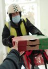 Mann mit Mundschutz und Helm liefert Pizza aus — Stockfoto