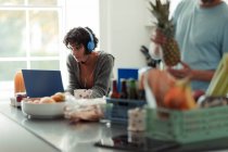 Жінка з навушниками, що працюють з дому на ноутбуці на кухні — стокове фото