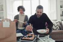 Paar genießt Essen zum Mitnehmen mit Essstäbchen im Wohnzimmer — Stockfoto