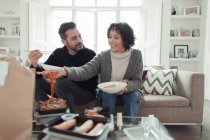 Felice coppia godendo cibo da asporto con bacchette sul divano del soggiorno — Foto stock