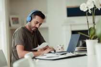 Mann mit Kopfhörern und Quittungen bezahlt Rechnungen am Laptop — Stockfoto